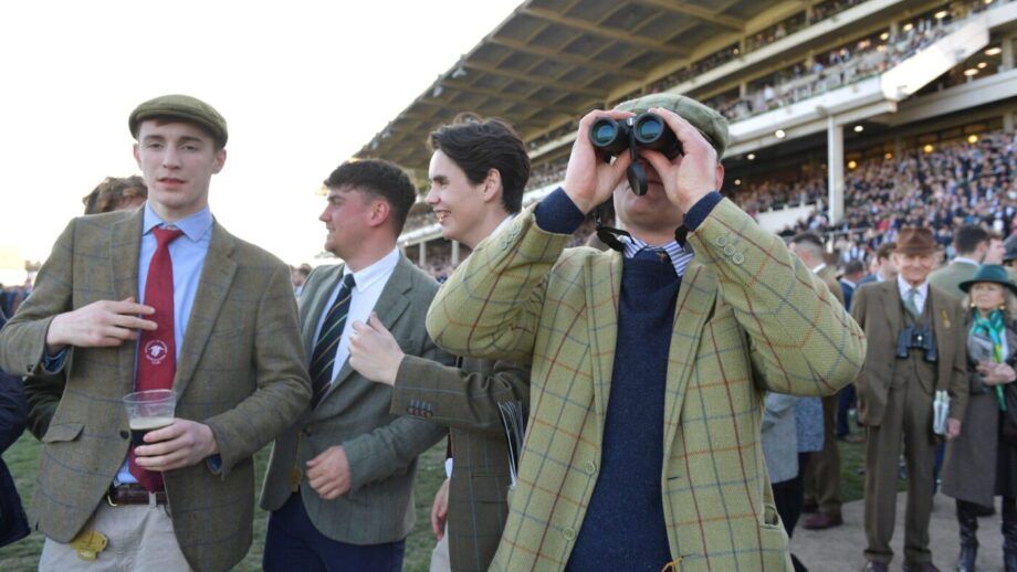 Four young male racing fans, one looking through binoculars at Cheltenham racecourse.