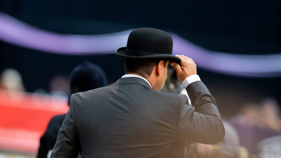 A judge with his hand on the front of his bowler hat and wearing a suit pictured from behind while judging at HOYS