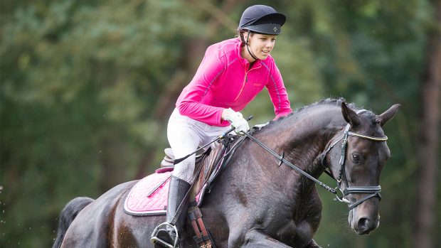 Woman jumping horse in a bright pink base layer