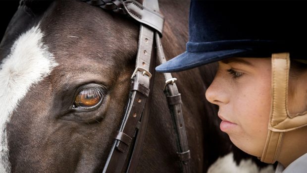 Girl wearing velvet riding hat up close with her horse’s head