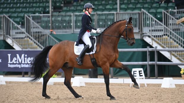 Laura Tomlinson canters a bay horse in an outdoor arena at the national dressage championships